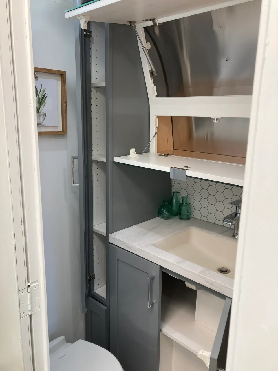 Open upper and lower vanity cabinets showing storage in the compact Airstream bathroom.