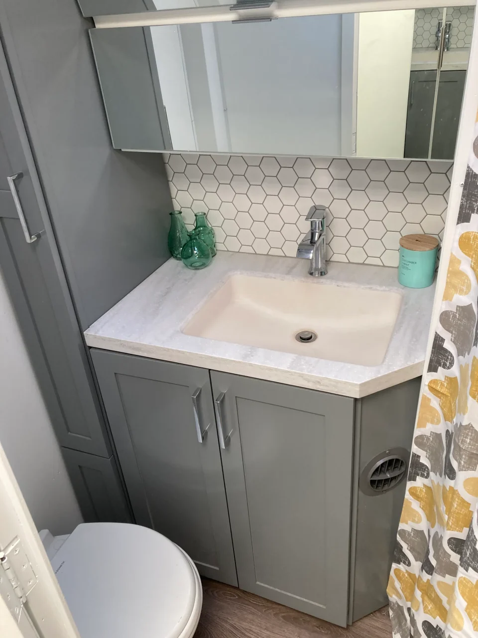Gray vanity with a white sink, hexagonal tile backsplash, and mirrored cabinet in the renovated Airstream.