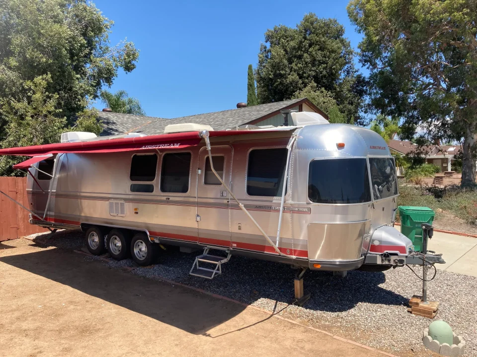 Renovated silver Airstream trailer with a red awning extended over its side entrance.