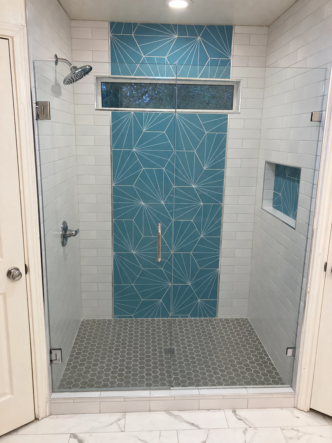 Completed shower with a blue geometric accent wall, white subway tile and a glass enclosure