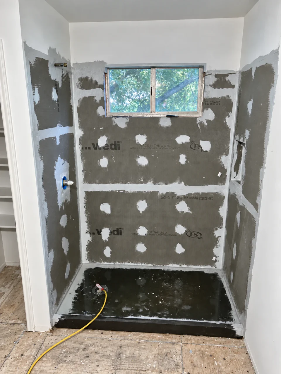 Sealed shower wall boards and a water-filled shower pan during flood testing before tile installation.