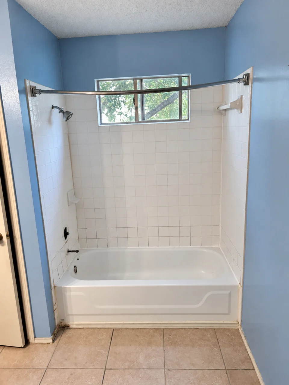 Before renovation: a bathtub with square white shower tile, blue painted walls and a curved curtain rod.
