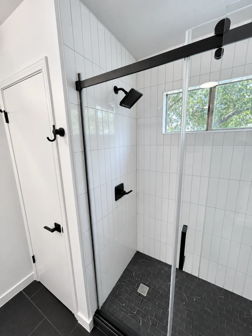 Close view of black sliding-glass shower hardware and a square showerhead against vertical white tile.
