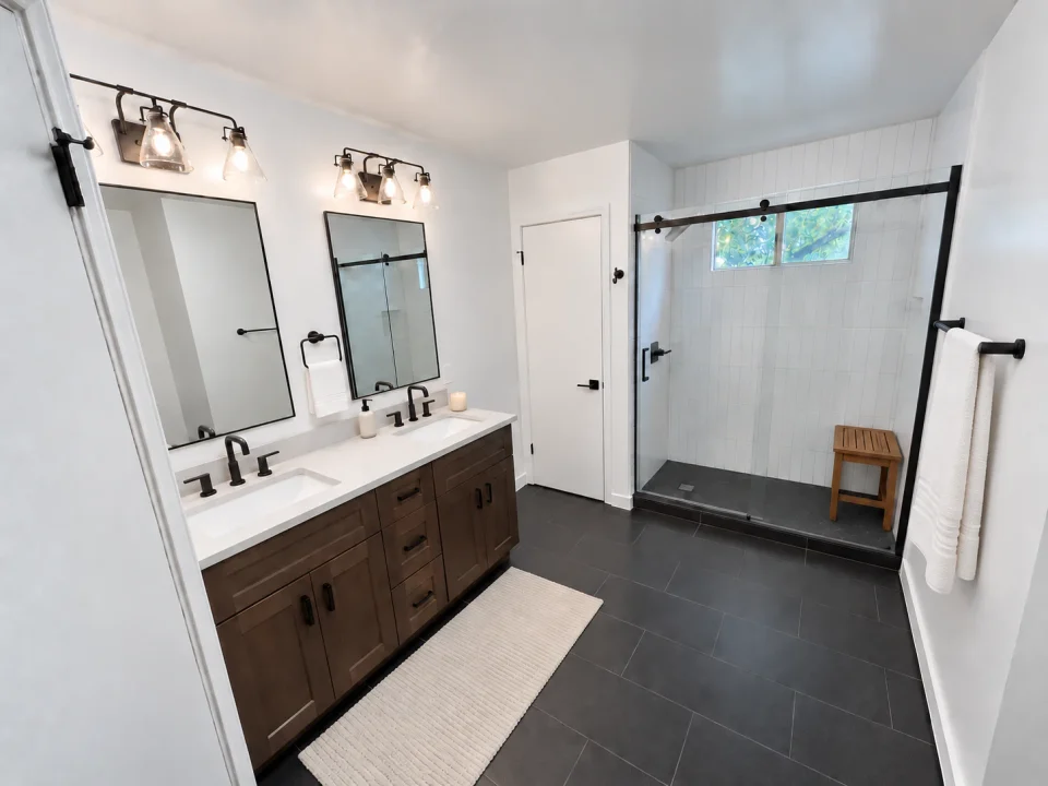 Brown wood double vanity with white counters beside a white-tiled shower with black sliding-glass hardware.