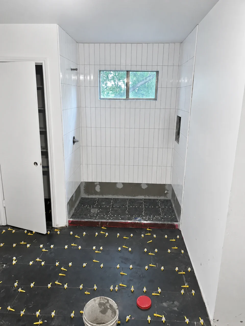 Dark bathroom floor tile with leveling spacers beside the shower during tile installation.