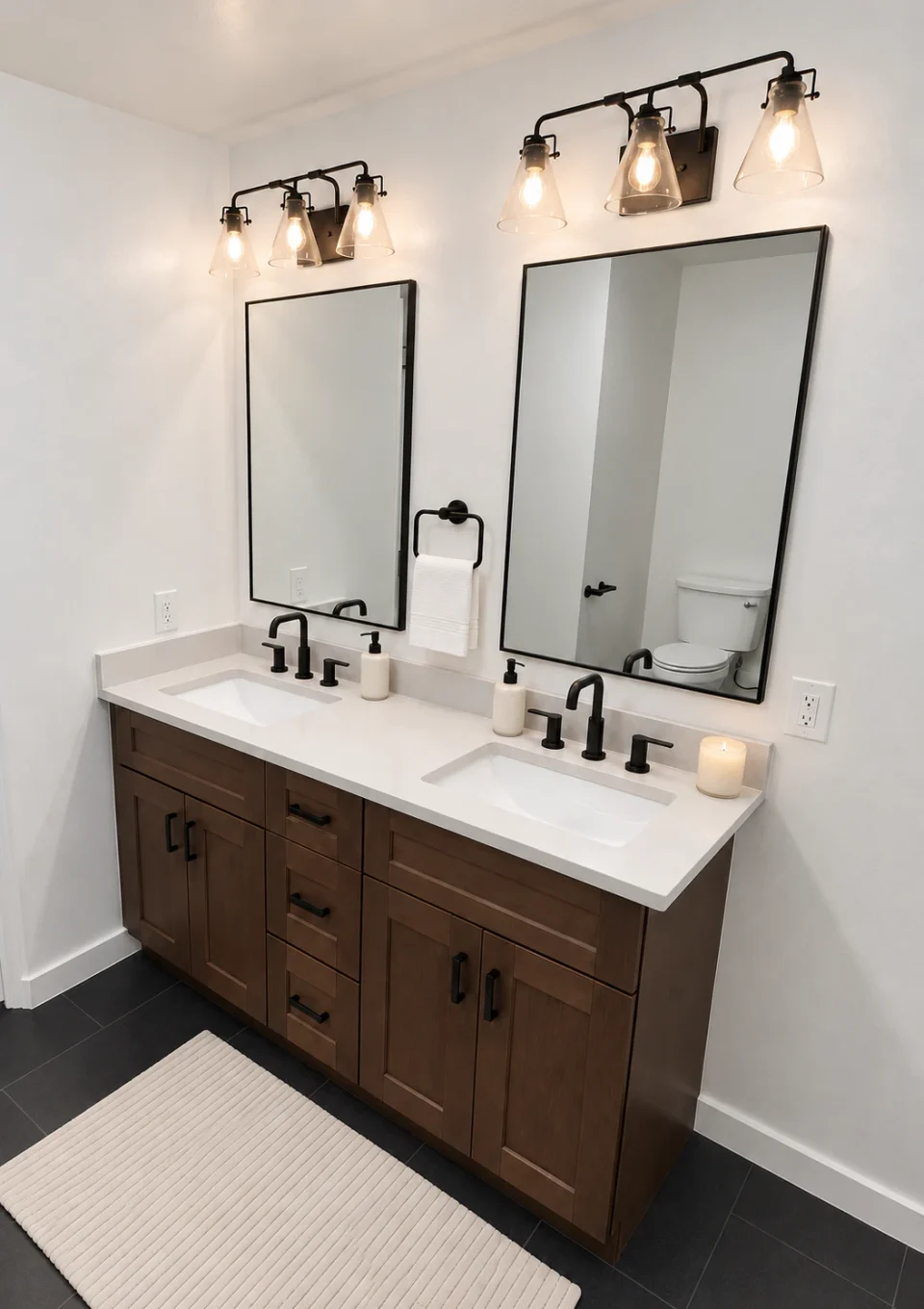 Brown wood double vanity with a white countertop, two black-framed mirrors, black faucets and a white hand towel.