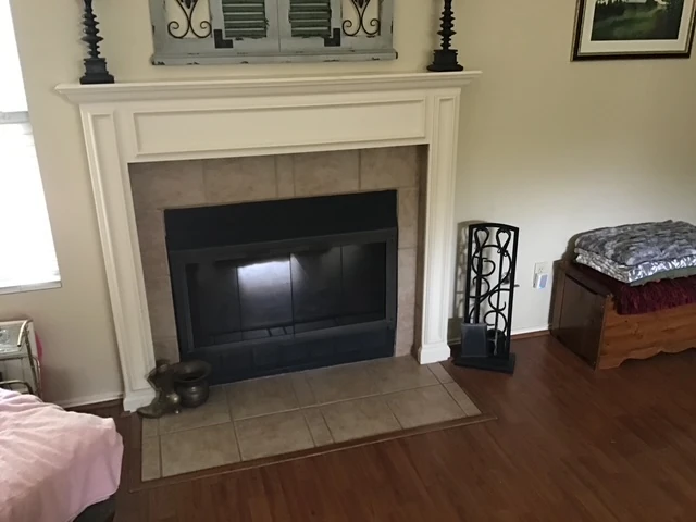 Fireplace before renovation with a white mantel, beige square-tile surround and tiled hearth.