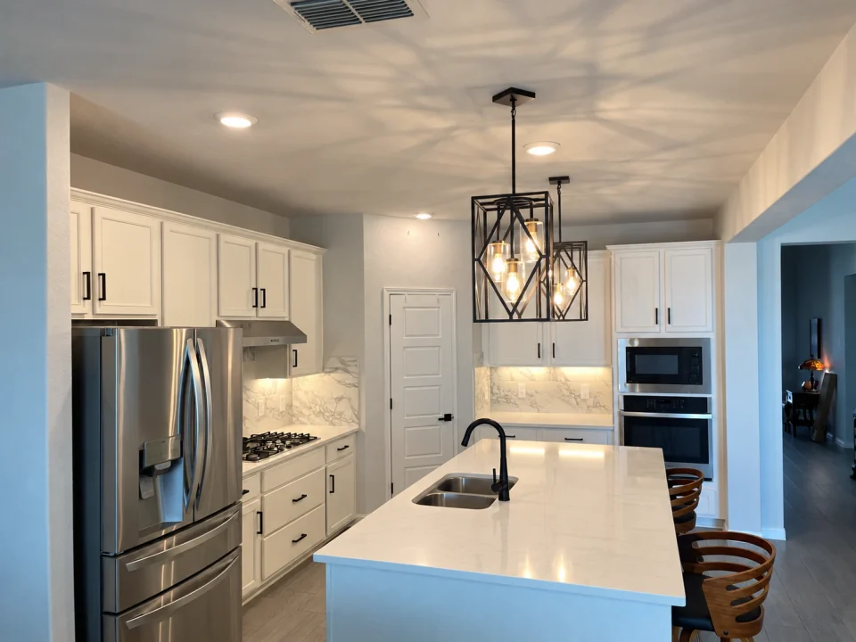 Before the refresh: white kitchen cabinets and a plain painted island beneath black geometric pendant lights.