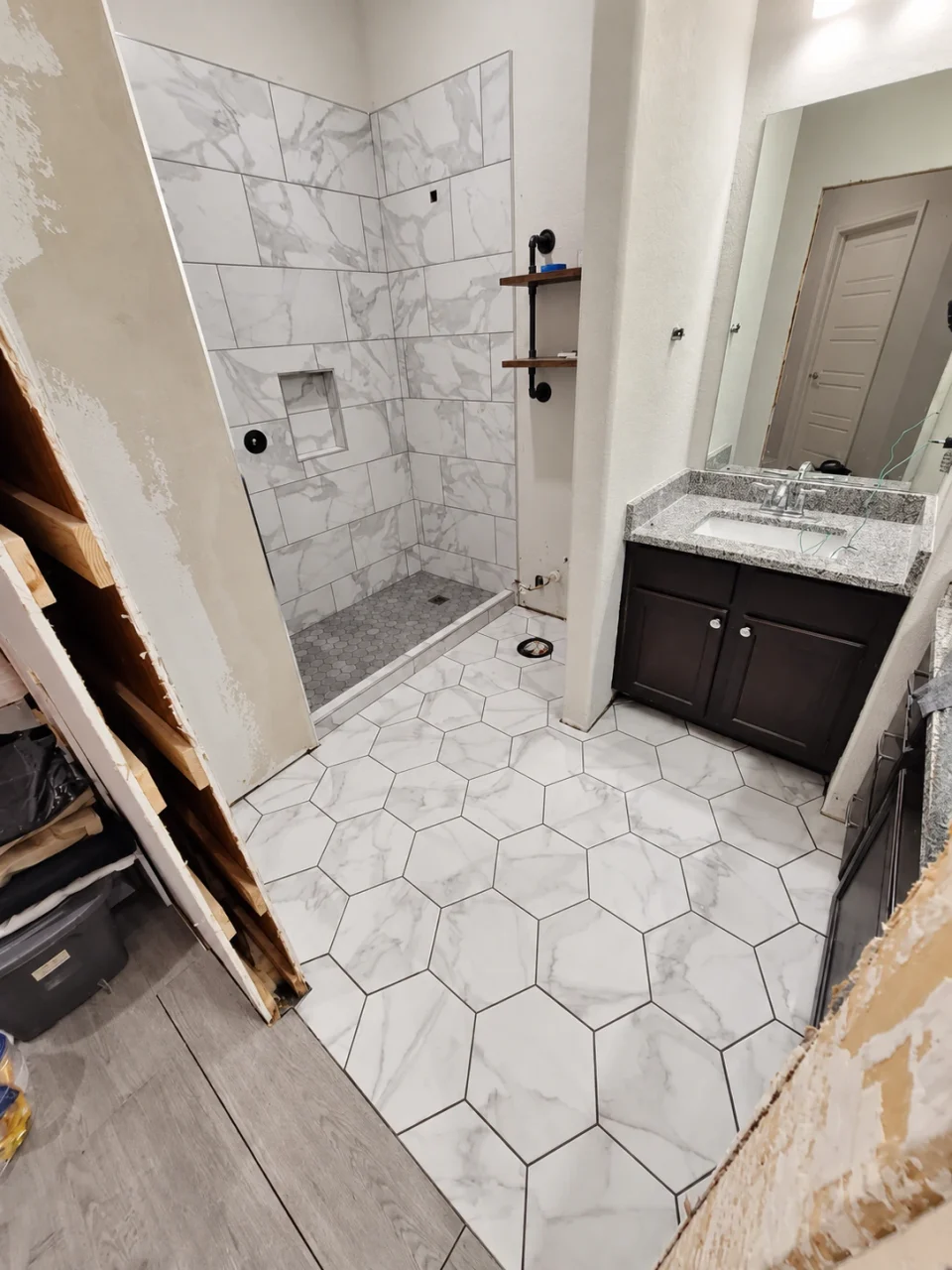 Bathroom in progress with exposed framing at the widened doorway, an enlarged shower opening and newly installed tile