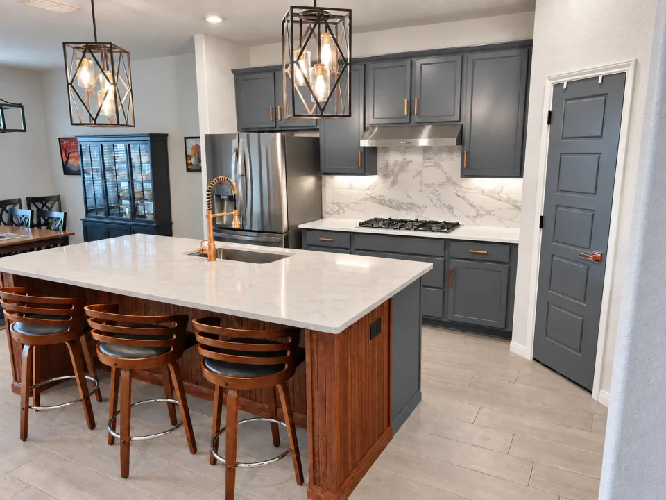 Wood kitchen island with a white countertop and bar stools, facing gray cabinets beside the dining area