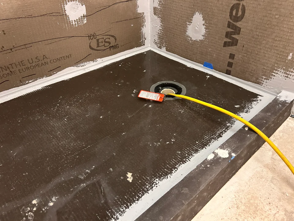 Shower pan during a flood test with sealed wall joints, a drain test plug and yellow hose