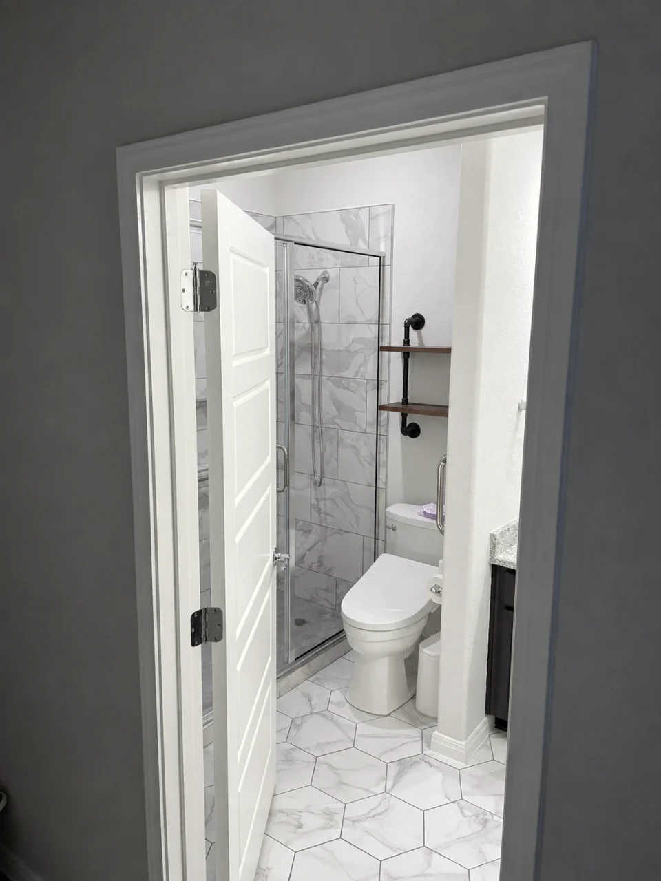 View through the widened bathroom doorway toward the new glass shower and hexagonal floor tile