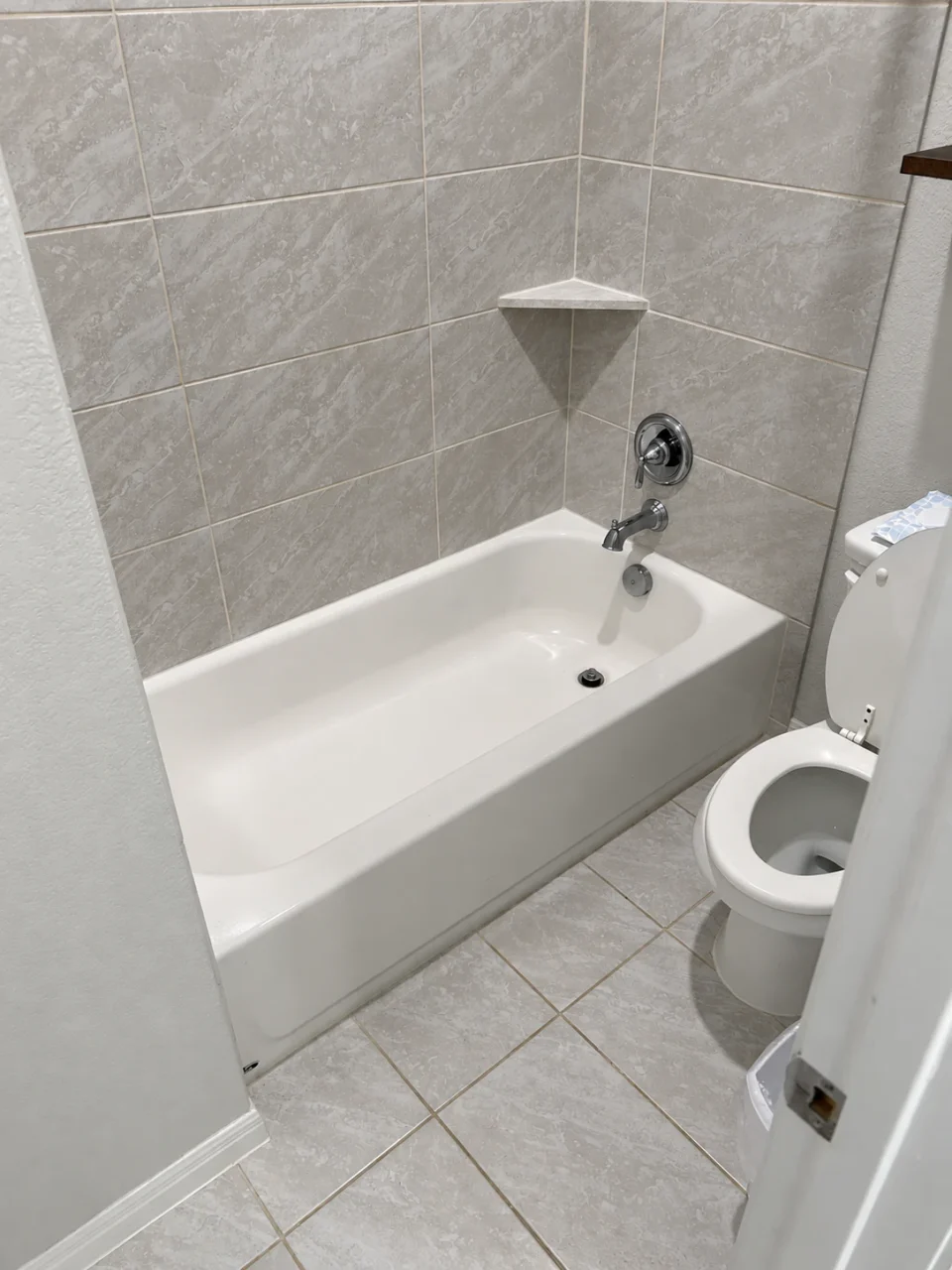 Original bathtub and tiled surround beside the toilet before the accessibility renovation