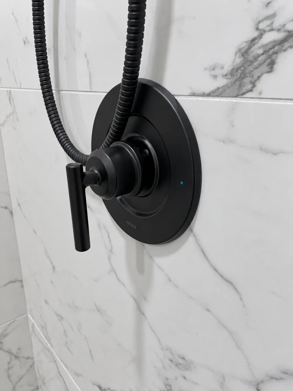 Black shower valve against marble-look wall tile
