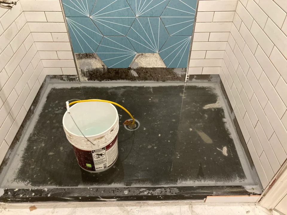 Water-filled shower pan during a flood test beneath the blue geometric wall tile