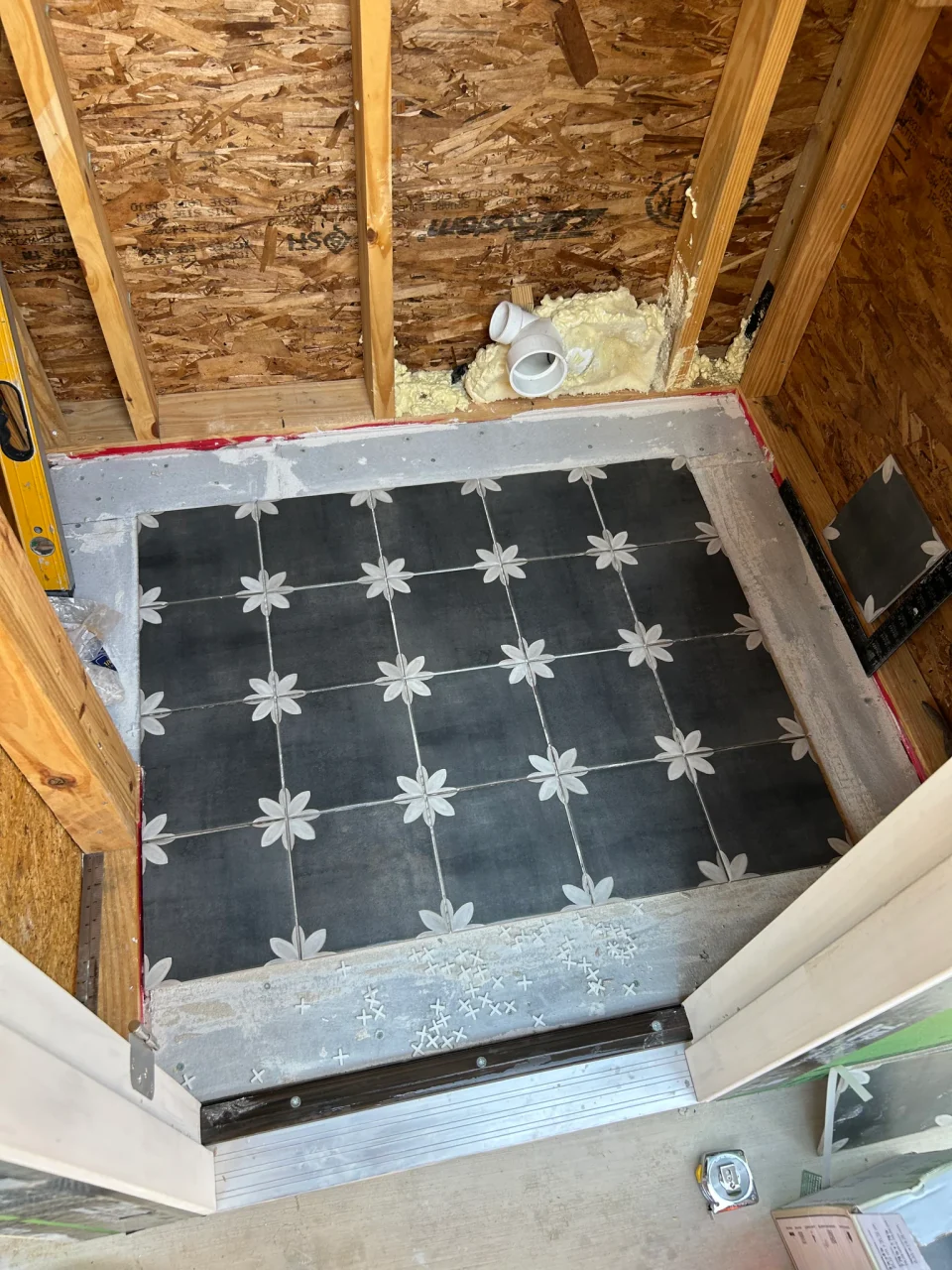 Custom freestanding outdoor powder room during construction, with patterned floor tile installed and unfinished walls.