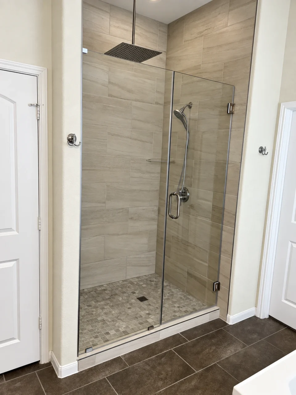 Frameless glass shower with warm-toned wall tile and an open mosaic floor