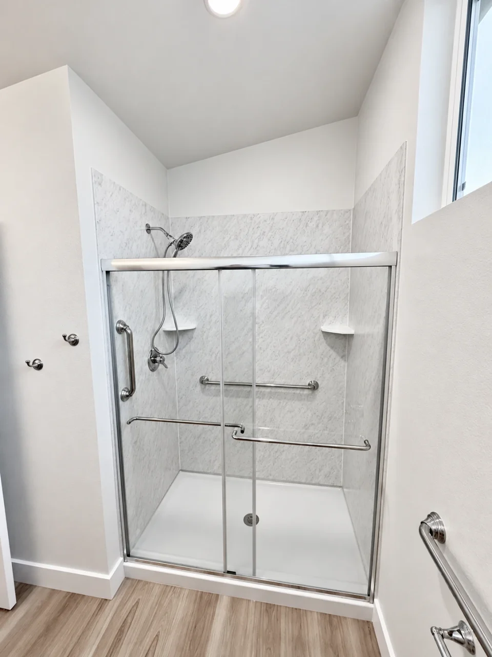 Detached ADU shower with Wilsonart Wetwall wall panels, glass shower doors, and a window.