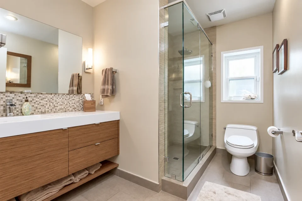 Floating wood vanity beside a glass-enclosed tiled shower