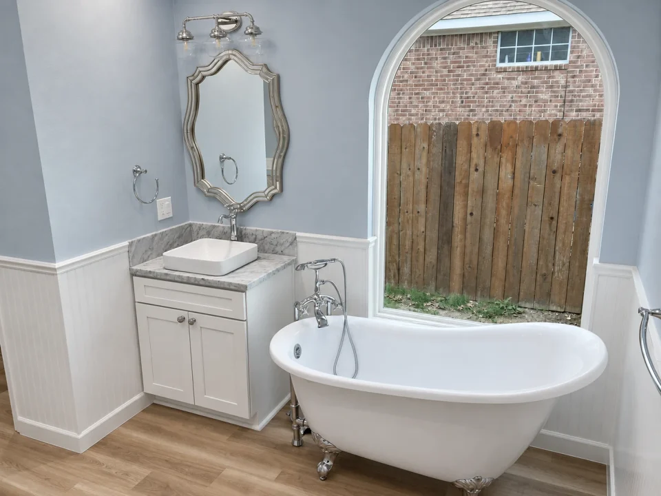 Clawfoot bathtub beneath an arched window beside a vanity