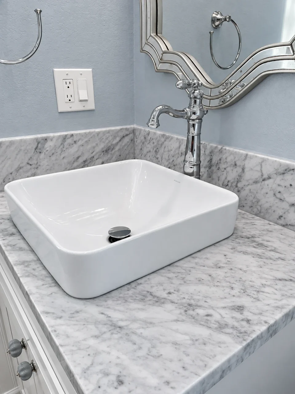 White rectangular vessel sink on a gray-veined stone countertop with a decorative mirror