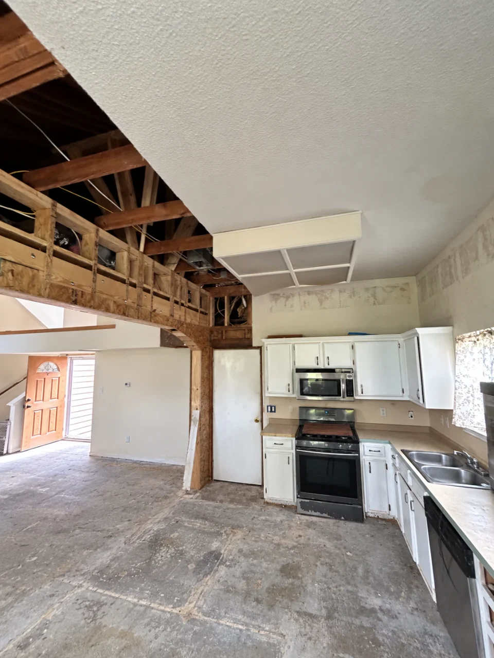 During renovation: original white cabinets, range and sink beside exposed wall and ceiling framing