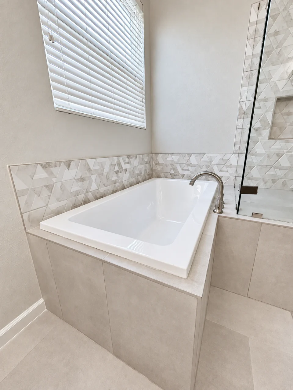 Bathtub beneath the window beside the textured-tile shower